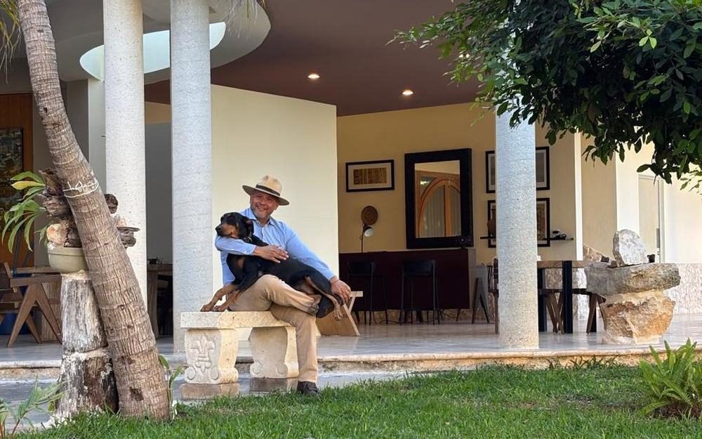 Un perro recostado en brazos de una persona, sentados en una banca del jardín del Palacio