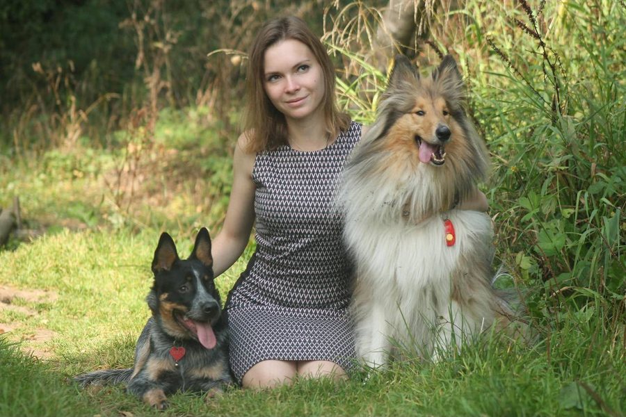 Masha Karpenko sentada en el pasto entre dos perros, un pastor ganadero y un collie